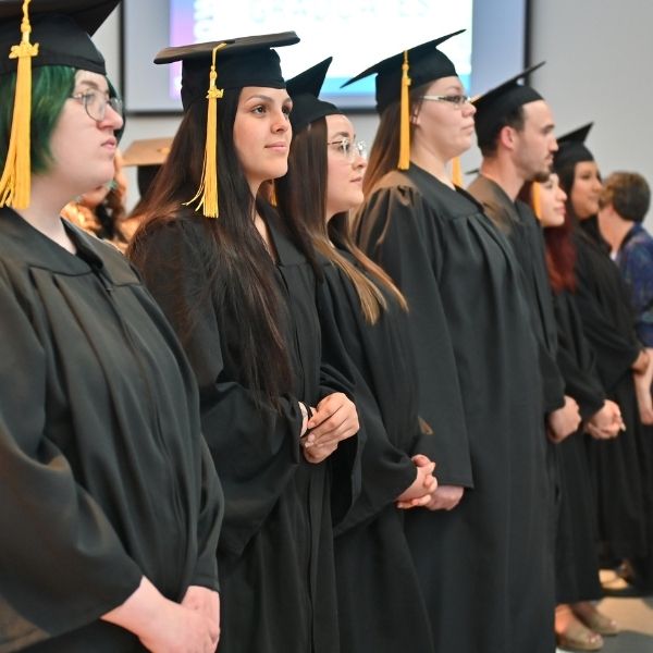 A row of graduate in cap and gowns stand during the graduation ceremony.