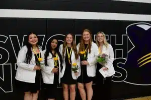 five Ellsworth nursing students wearing white jackets holding flowers upon passing exams
