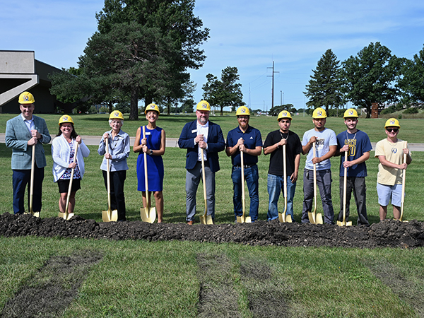 ten people wearing hard hats and holding golden shovels standing behind a mount of dirt on the MCC campus