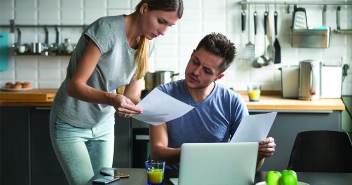 couple-sitting-in-kitchen-talking-over-computer